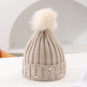 Close-up of beige knit beanie with fluffy faux fur pom-pom and elegant pearl decorations
