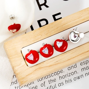 Cute red apple stud earrings with heart detail and zircon inlay on a wooden stand