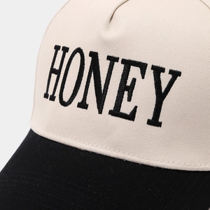 Gros plan détaillé de la broderie HONEY et de la texture sergé sur la casquette bicolore