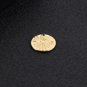 Golden stainless steel circular pendant with engraved eye and sunburst on black background