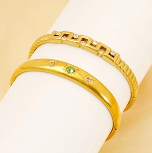 Detail of gold-plated bracelets featuring Greek key patterns and star-engraved gemstones