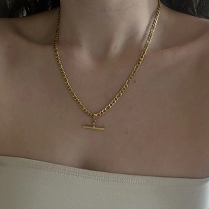 Close-up of golden Figaro chain necklace featuring a modern T-bar toggle clasp on model