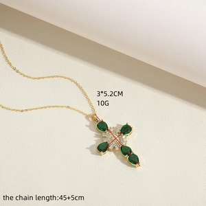 Close-up of gold cross necklace with green teardrop gemstone and white zircon stones