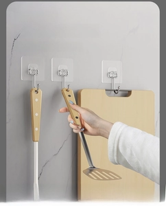 Strong transparent adhesive wall hooks holding wooden kitchen utensils on marble surface