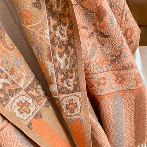 Close-up of floral jacquard fabric texture and tassel detail on an orange ethnic shawl