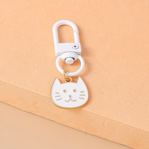 Close-up of a white cat metal keychain with gold trim and a D-shaped clasp on orange background