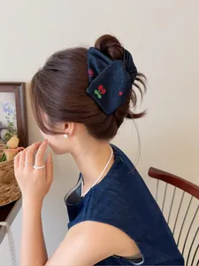 Détail d'une pince à cheveux en denim bleu marine avec broderie cerise sur le côté
