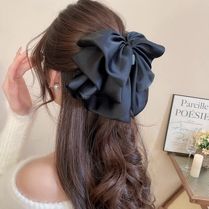 Detail of elegant black satin oversized bow hair clip worn on model in a cozy setting