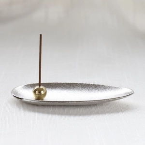 Macro detail of silver boat-shaped incense tray and golden spherical holder with zen aesthetic