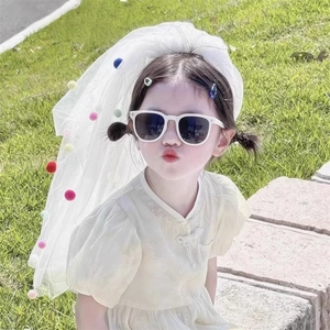 Detail of white mesh veil with colorful pom-poms for girls on a sunny outdoor day