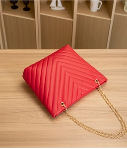 Detail of red V-quilted faux leather tote bag with gold chain strap on a wooden surface