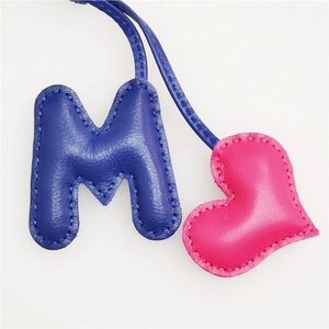 Detail of handmade leather bag charm with blue letter M and pink heart shaped pendant