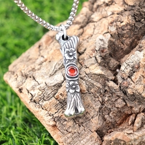 Macro shot of vintage silver-tone floral carved pendant with a red gemstone on tree bark
