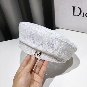 Close-up of white lace beret featuring floral hollow patterns and a gold metal M detail