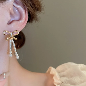 Detail of elegant gold bow earrings with dangling pearl tassels worn by a female model