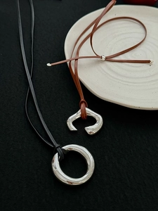 Polished silver ring pendants on black and brown leather cords over white ceramic