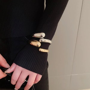 Polished gold and silver teardrop open bangles shown on wrist with black knit sweater