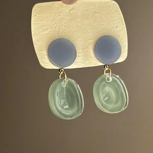 Detail of resin earrings featuring grey-blue circular stud and light green drop pendant
