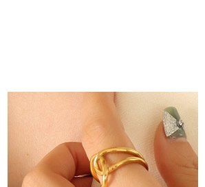 Detail shot of a minimalist gold twisted knot ring worn on a finger against beige background