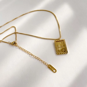 Macro shot of 18K gold sun square pendant necklace with lobster clasp on white surface