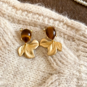 Close-up of goldfish earring with pear-shaped resin stone on a beige knitted background