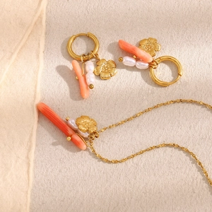 Detail of 18K gold plated jewelry set with pink stones and white pearls on beige fabric