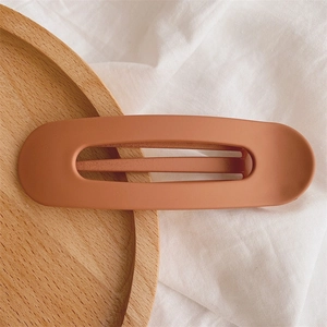 Detail of matte caramel orange duckbill hair clip on a minimalist wooden tray