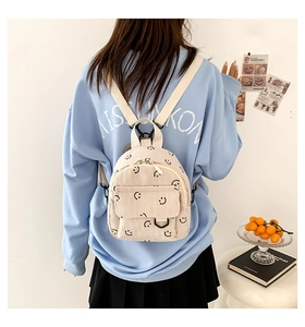 Nahaufnahme eines beigen Mini-Rucksacks aus Cord mit aufgesticktem schwarzen Smiley-Motiv