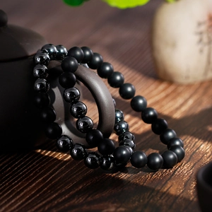 Minimalist stackable matte black onyx and hematite beaded bracelets for men on a ceramic teapot
