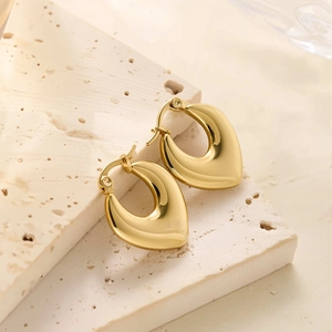Vue macro détaillée des boucles d'oreilles goutte dorées 18k sur surface en pierre beige