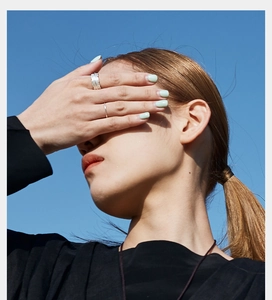 Detail of silver angel wing feather rings worn by a model against a bright blue sky background