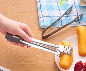 Close-up of stainless steel food tongs with serrated edges on a wooden dining table
