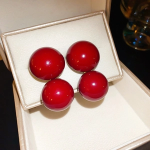 Close-up of vibrant red spherical stud earrings on a cream-colored jewelry display pad