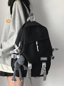 Black canvas backpack with white letter straps and a gray frog plush worn by model