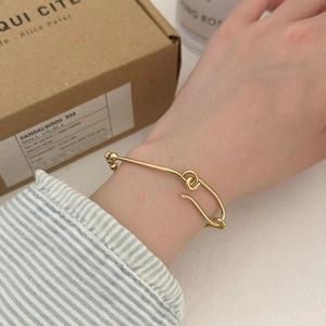 Detail of a minimalist gold safety pin bracelet worn by a model in a warm setting