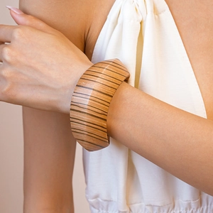 Detailed close-up of wide wooden bangle with horizontal stripes on model's wrist