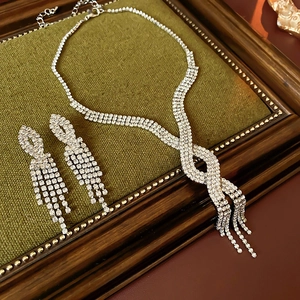 Silver rhinestone necklace and earrings set with fringe tassels on green background