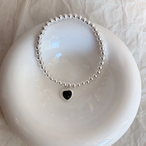 Minimalist silver beaded bracelet with a black heart pendant on a white ceramic tray