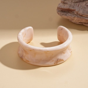 Détail du bracelet ouvert en résine marbrée beige sur fond de sable chaud et de roche