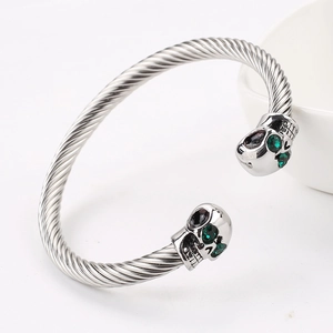 Detailed shot of silver skull cuff bracelet with green gemstone eyes on white ceramic bowl
