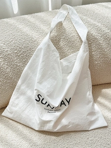 Minimalist white tote bag with Sunday print on textured fabric shown on a sofa