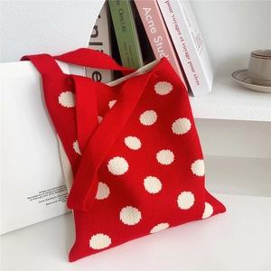 Dettaglio borsa shopper in maglia rossa a pois bianchi su uno scaffale bianco minimal