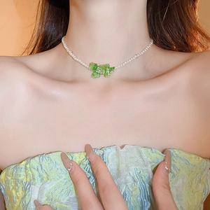 Close-up of pearl necklace with a light green crystal flower pendant on a model