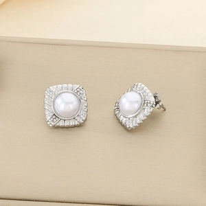 Détail macro de boucles d'oreilles argentées avec perle blanche et cadre en zircon
