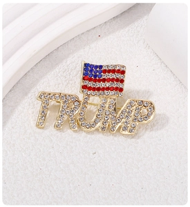 Detail of a gold-plated TRUMP letter brooch with American flag and inlaid crystals
