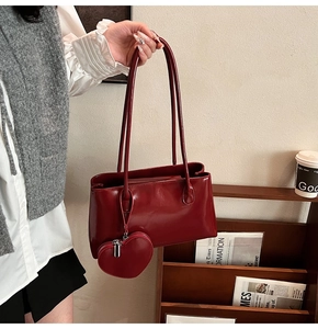 Detail of dark red patent leather shoulder bag with a matching heart charm accessory