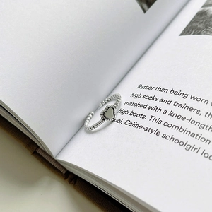 Close-up of vintage 925 sterling silver beaded ring with a heart charm on book pages