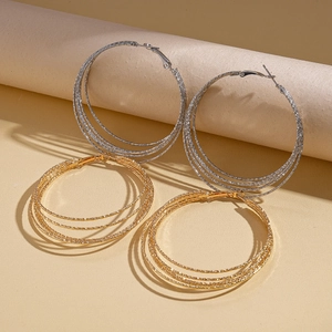 Mehrlagige geometrische Gold- und Silber-Creolen mit strukturierter Optik auf Papierrollen