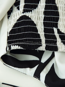 Detailed macro view of smocking craft on black and white abstract print dress fabric
