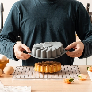 Gray sunflower silicone cake mold held in hand for home baking in a warm kitchen setting